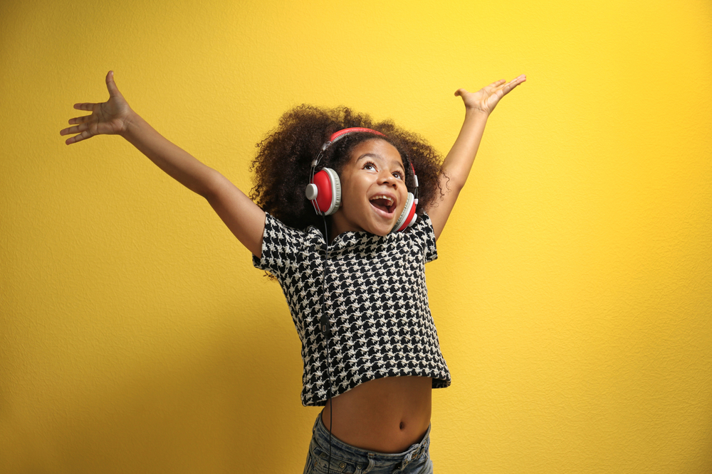 Afro-American little girl with headphones on yellow background