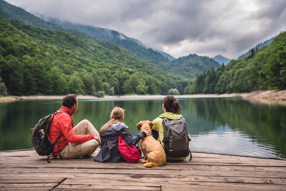 Family with a small yellow dog looking out over a lake surrounded by mountains