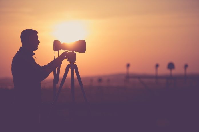 Men Taking Outdoor Pictures During Scenic Sunset. Photographer Silhouette. Telephoto Lens and the Modern Camera on a Tripod.