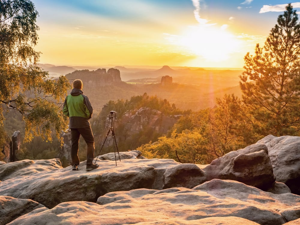 Man photographer staring into misty landscape of Saechsische Schweiz park. Beautiful evening at Schrammsteine pass, view over sandstone cliff into deep misty valley