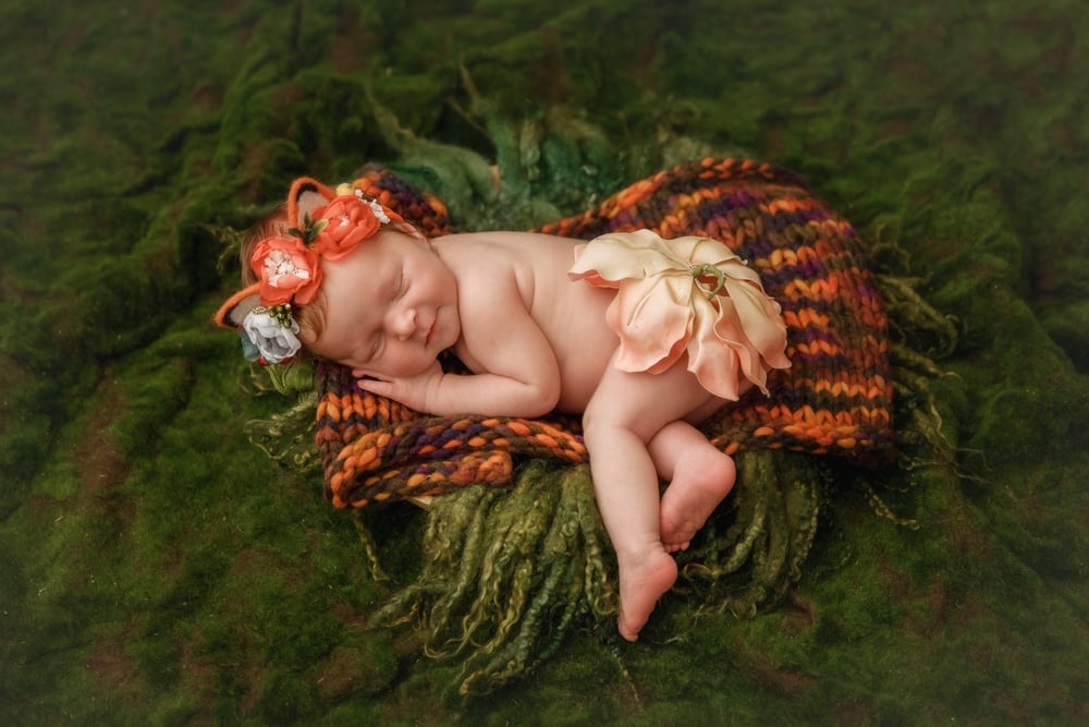 Newborn baby in cute fox outfit sleeps in a green forest with moss and grass set up in studio