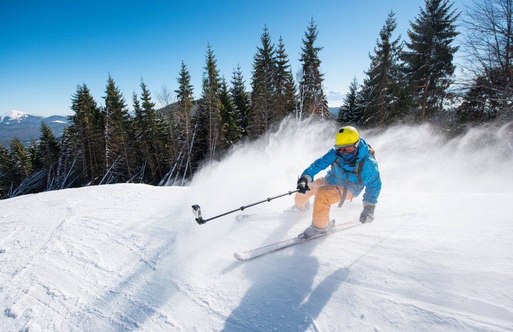 Action shot of professional skier taking selfies photo with a camera on selfie stick while skiing on fresh powder snow in the mountains at the winter resort Bukovel