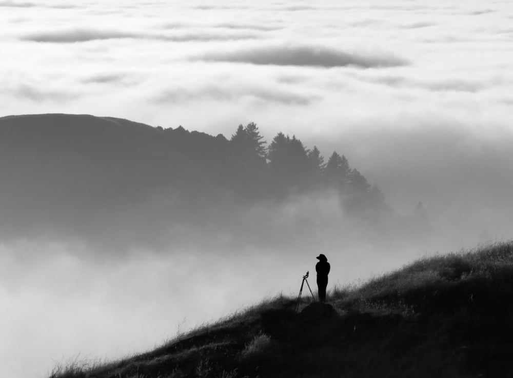 Silhouette of photographer overlooking a blanket of fog