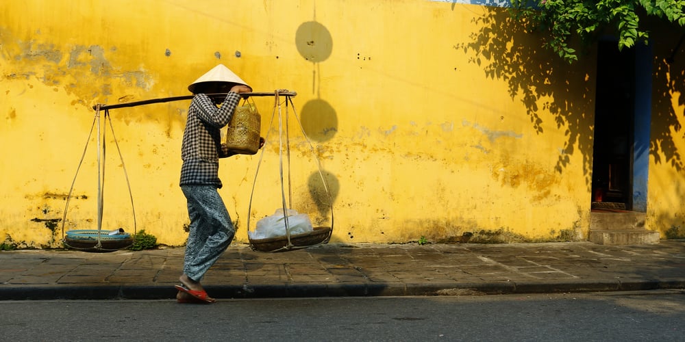 Street Merchant in Vietnam walking by yellow wall