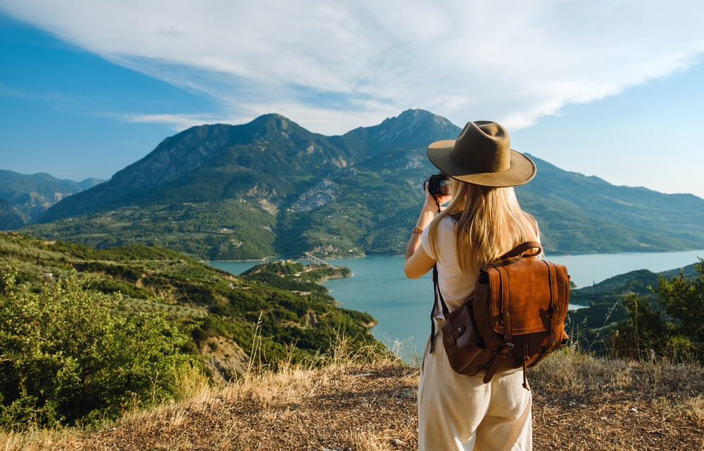 Woman photographer with big backpack taking photo of mountains and blue lake.