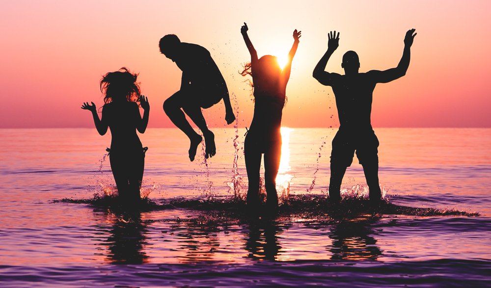 friends jumping in water on tropical beach at sunset  Silhouette