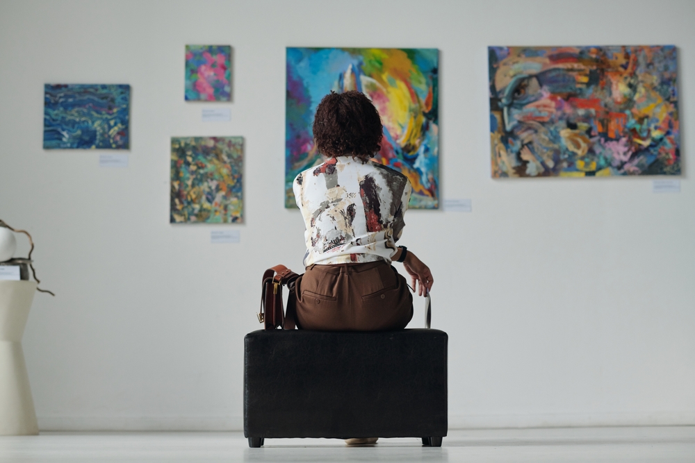 woman sitting on couch and looking at paintings on the wall