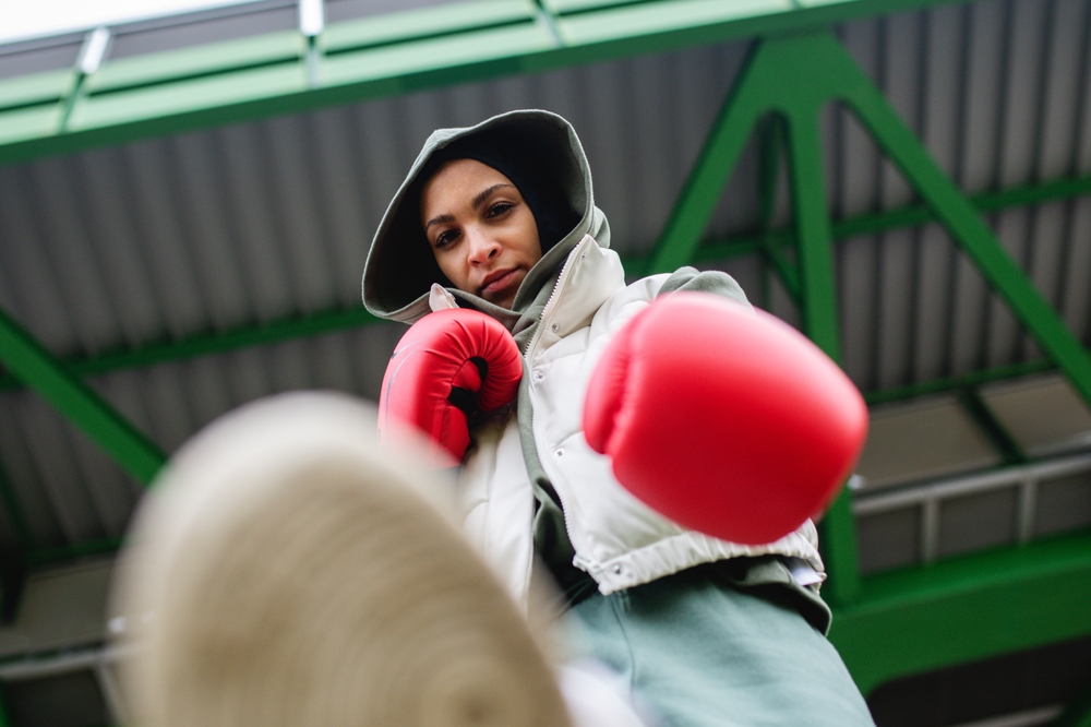 Low angle view of young muslim woman with boxing gloves standing outdoor in city.