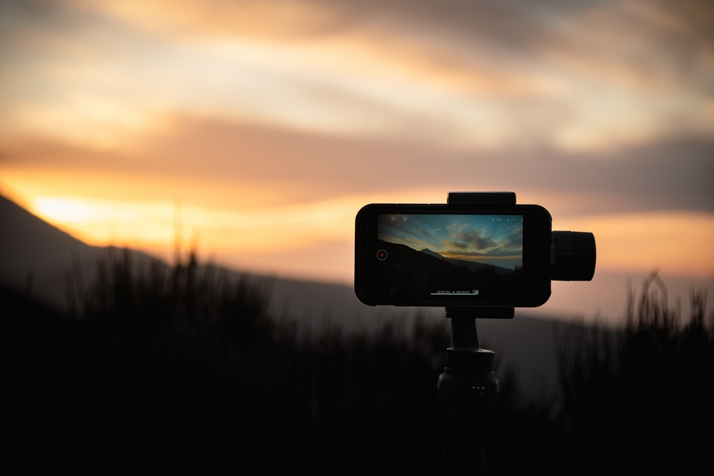 Smartphone on a tripod with active screen shooting sunset in the mountains.