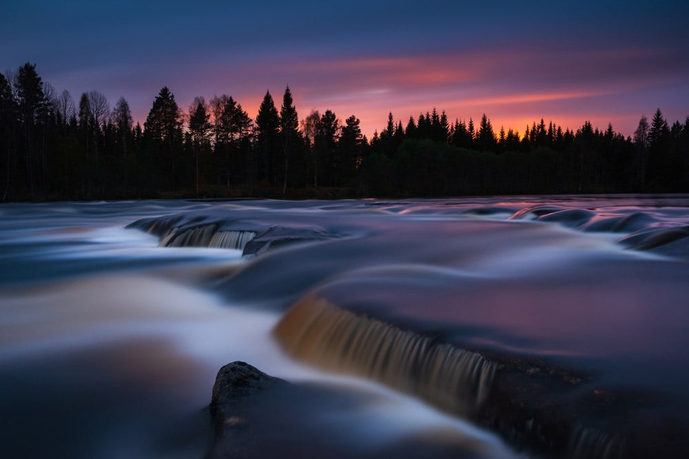 Misty water rushing over rocks at sunset