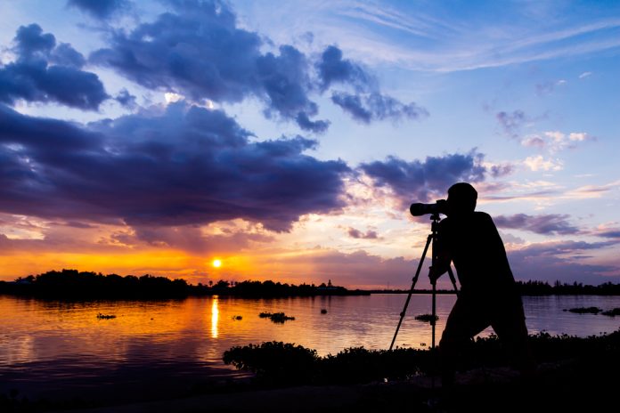 silhouette of photographer taking photo at sunset beside the river